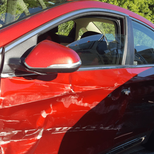 Close-up of a red car door damage from a car accident in Clearwater, showing the impact of a collision.
