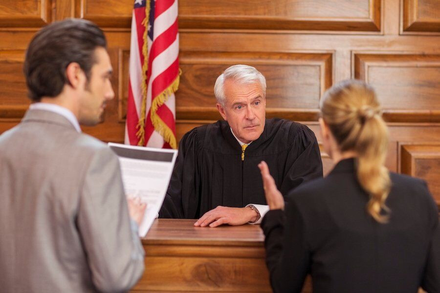 Two attorneys in discussion with a judge at the bench, with an American flag in the background.